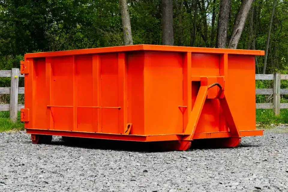 Compact orange roll-off dumpster on gravel
