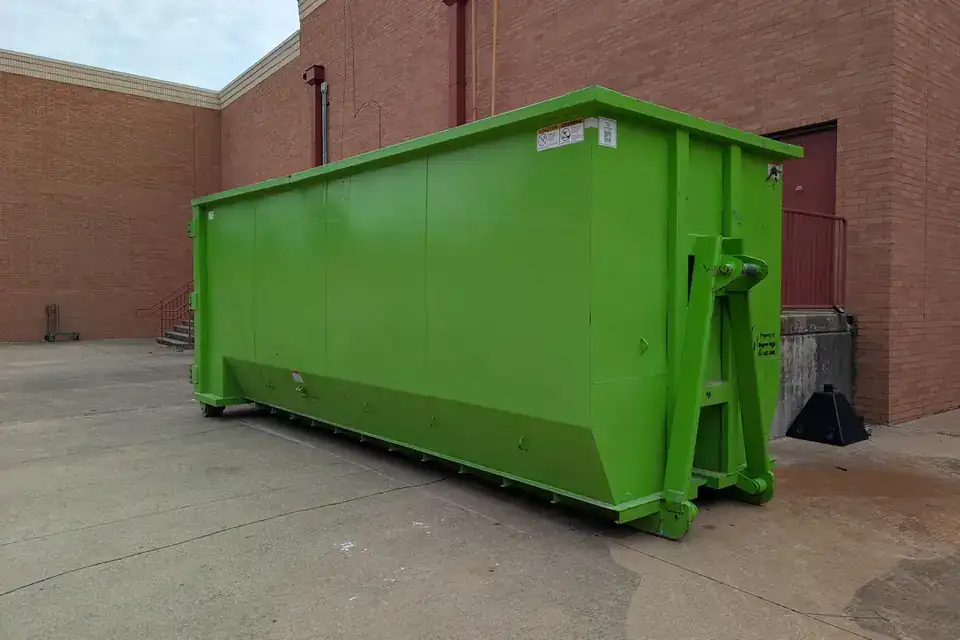 Long, tall green 30-yard style roll-off dumpster beside a commercial building